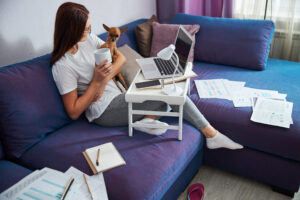 A young woman running her independent LNC practice from home on the couch holding her puppy. 